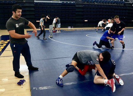 College champion Isaiah Martinez watches over a pair of young wrestlers.